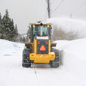 Yellow tractor spraying snow as it removes it from the roadway. 