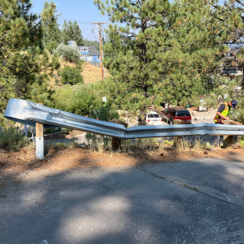 A damaged guardrail with a person in a yellow vest assessing it. 