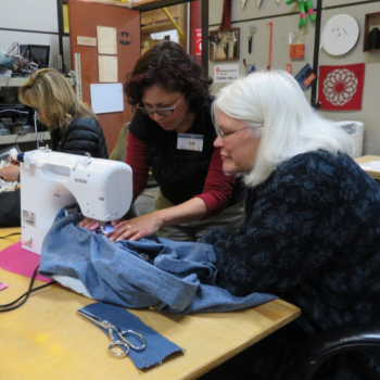 two women in a community workspace looking at an item in a sewing machine during a workshop. 
