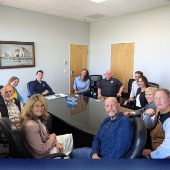 Group of people gathered around a table for meeting, smiling at the camera. 