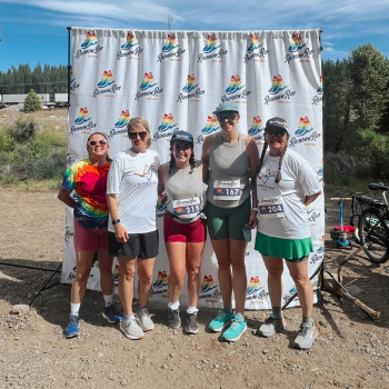 five female staff members stand in front of the Rainbow Run banner post-race. 