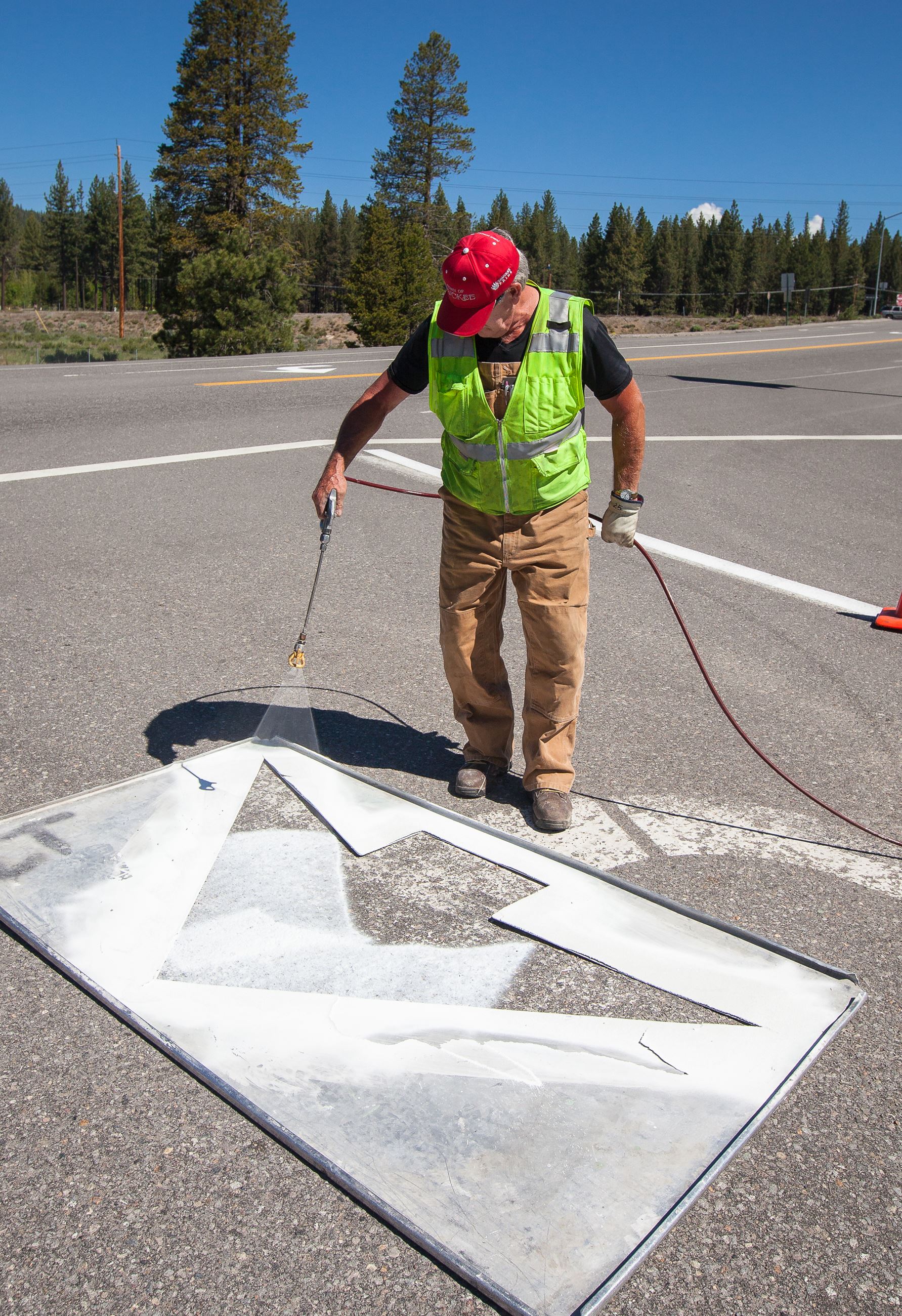 A road crew member paints a white left turn arrow on the road.